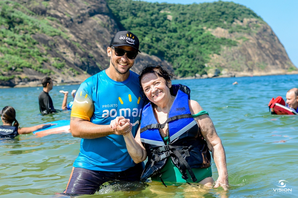 Voluntário e participante sorrindo dentro do mar, usando coletes salva-vidas do Projeto Ao Mar
